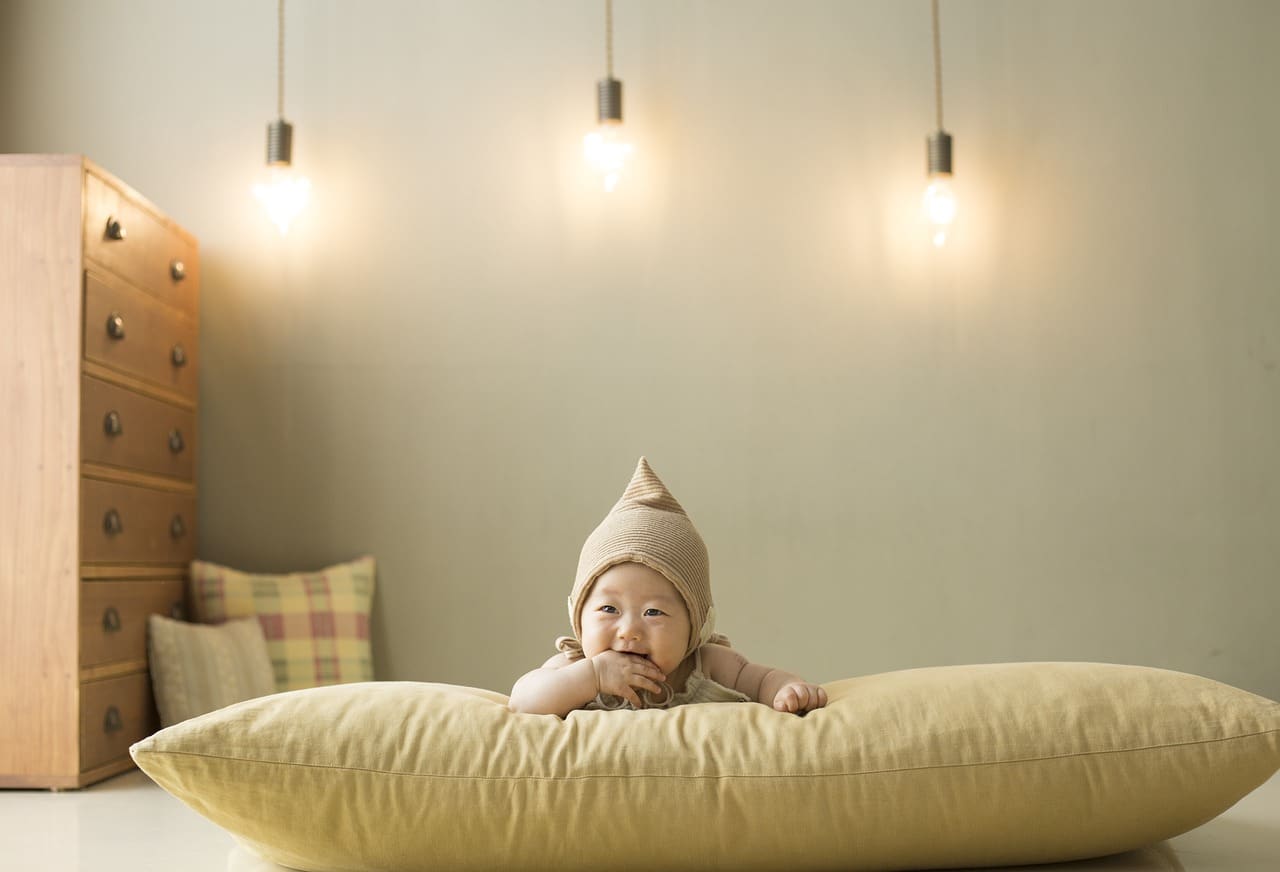 dziecko na jasnej poduszce na tle ściany i wiszących u góry lamp