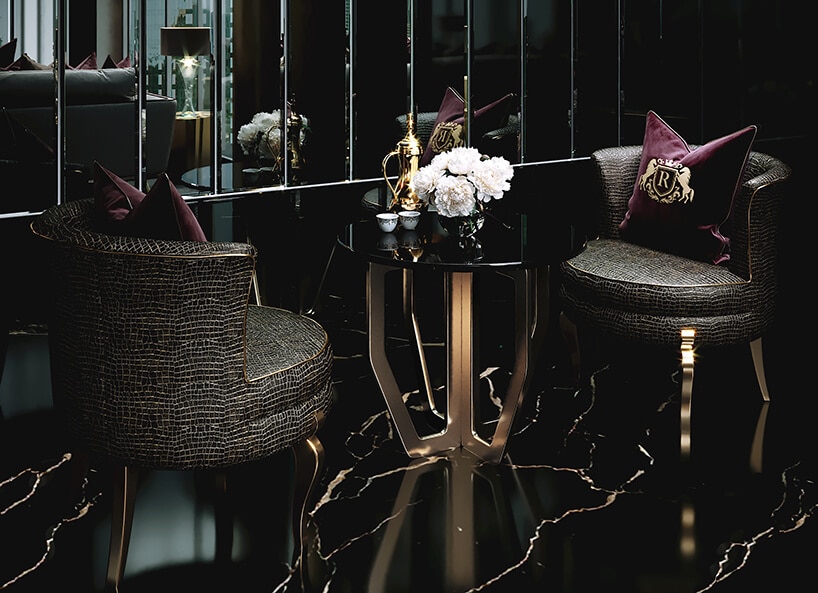 luksusowe wnętrze apartamentu w Dubaju od Covet House zielone fotele ze złotym wykończeniem i nogami przy czarnym małym stoliku ze złota podstawą na tle ciemnego pomieszczenia