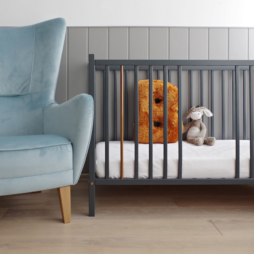 eleganckie szare łóżeczko od Woodies Safe Dreams z wyjętymi szczebelkami obok niebieskiego fotela