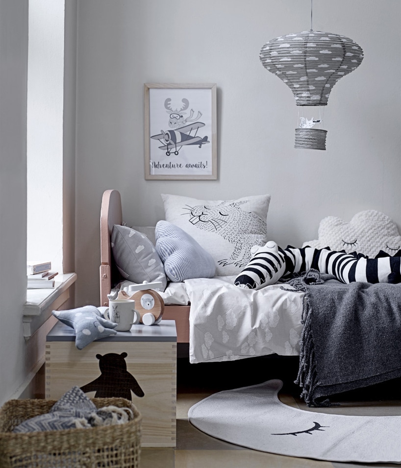 drewniane łóżko dziecięce obok drewnianej szafki pod lampą z żyrandolem w kształcie balonu
