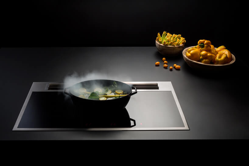czarna z metalową ramką płyta indukcyjna ze zintegrowanym okapem podczas gotowania podczas gotowania żółtych warzyw