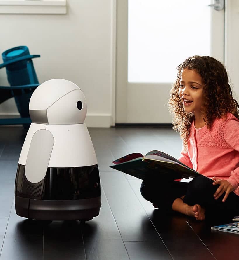 dziecko trzymające książkę i siedzące obok biało-czarnego robota