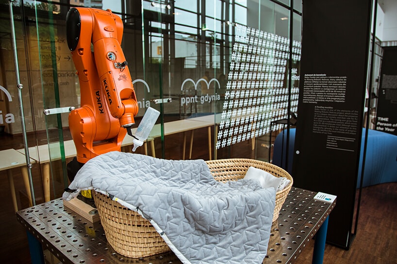 ramię robota automatycznego trzymające butelkę do karmienia dzieci na wiklinowym łóżeczkiem na Gdynia Design Days 2019