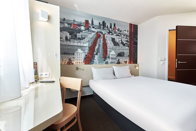 jasne wnętrze pokoju hotelowego duże łóżko na tle zdjęcia Warszawy