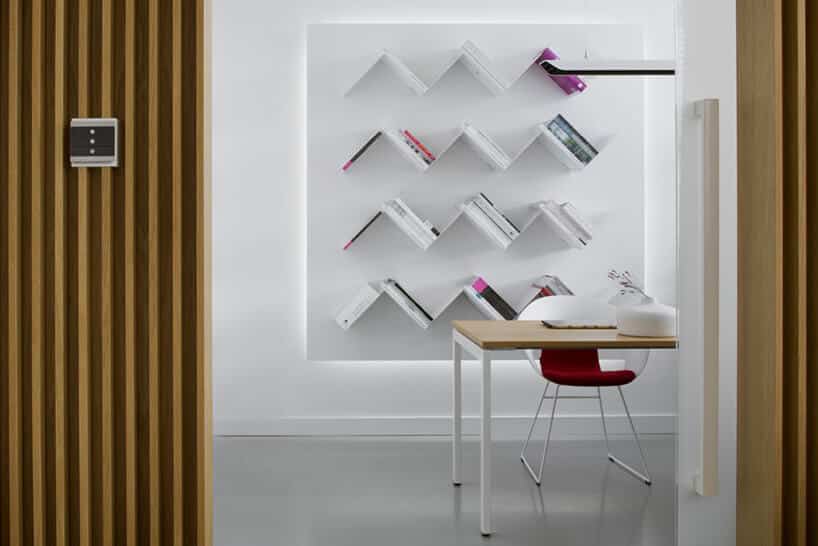 nowoczesne białe wnętrze małe biurko z czerwony krzesłem na tle ściany z trójkątnymi półkami na książki z panelem sterującym ABB na drewnianej ścianie