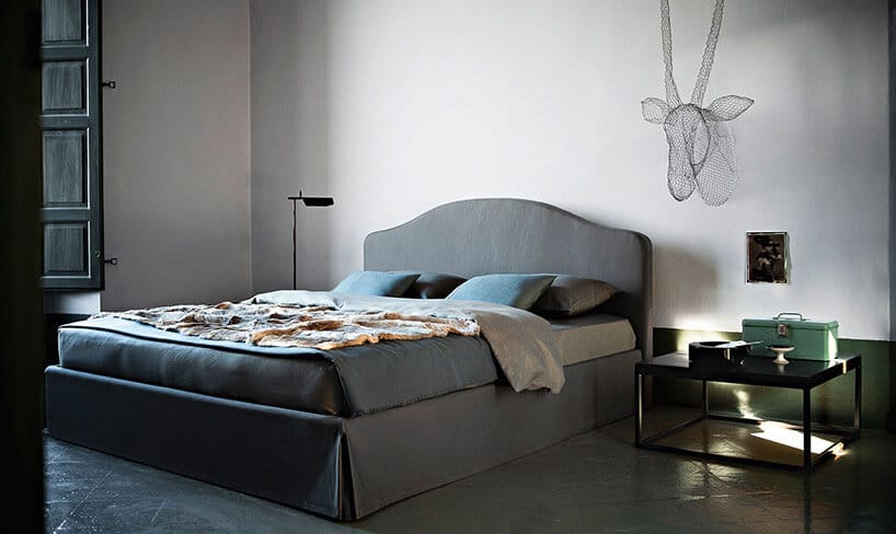 niebieskie łóżko czarny stolik nocny na tle białej ściany