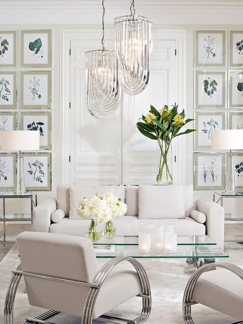 biała sofa i dwa fotele za szklanym stolikiem na tle białej ściany z obrazami