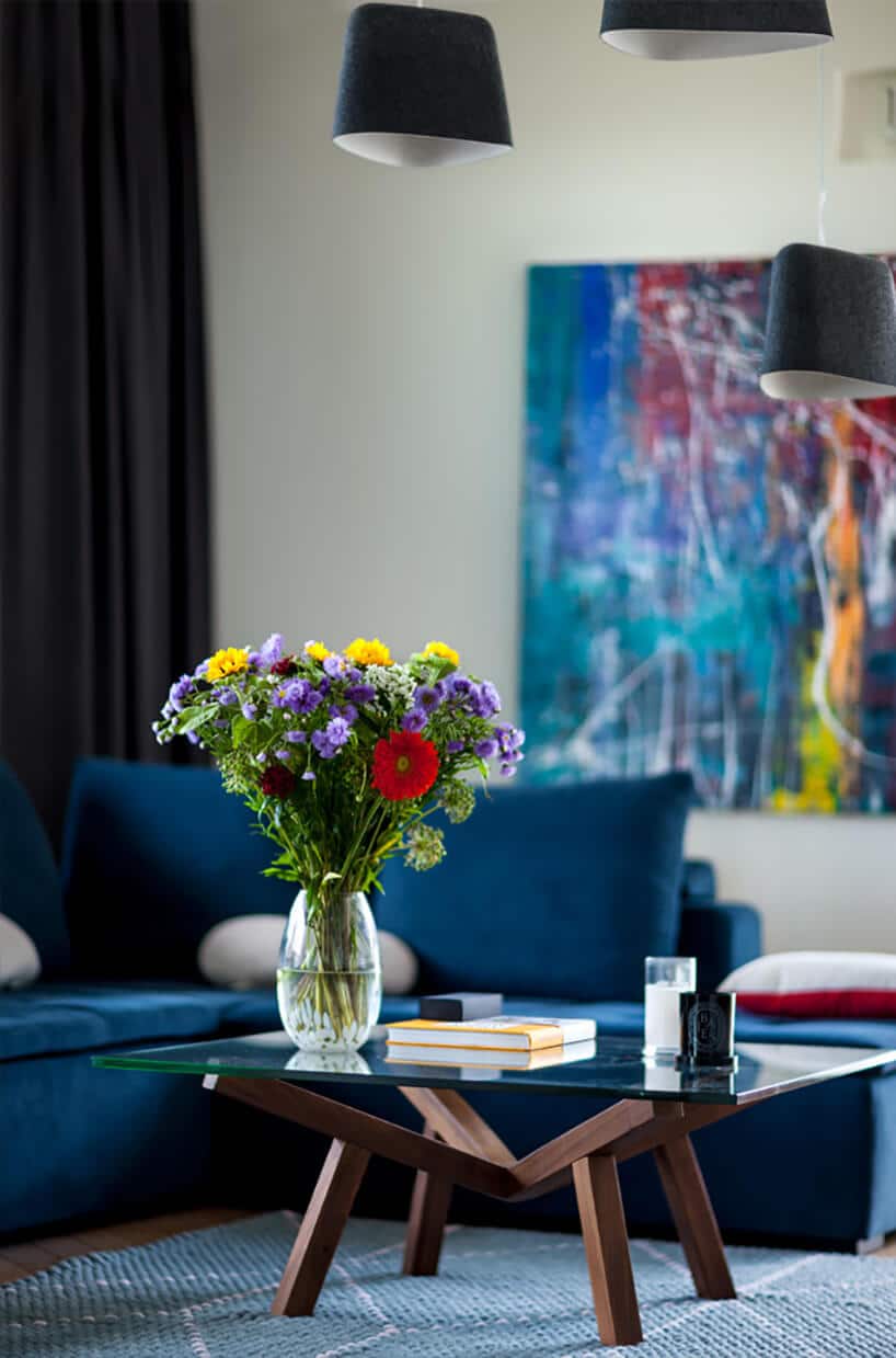 elegancki salon z ciemno niebieską sofa narożną jako tło dla niskiego stolika na drewnianym stelażu ze szklanym blatem