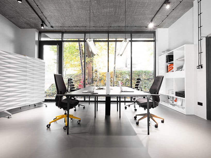 dwa biurka z krzesłami w białym biurze na tle przeszklonej ściany