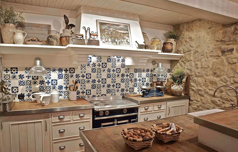 kuchnia w stylu prowansalskim z kamienną ścianą i z biało niebieskimi małymi płytkami nad drewnianym blatem z desek wykończoych