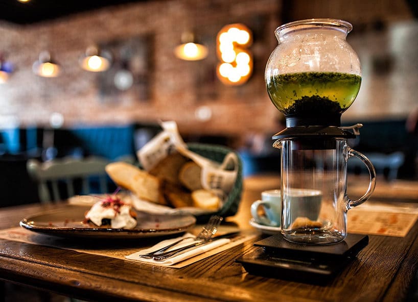 elegancki ciemny drewniany stolik w restauracji z nieregularnym talerzem obok zaparzacza na szklance