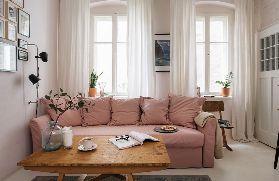 drewniany stolik na tle jasno różowej sofy na tle dwóch wysokich podwójnych okien