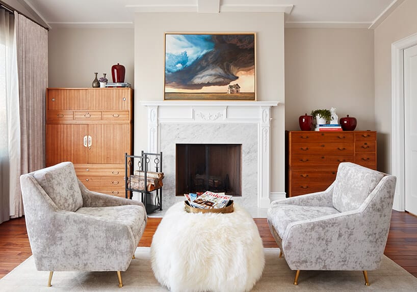modernistyczne wnętrze Ravenswood Residence elegancki salon ze zdobionym białym kominkiem dwoma szarymi fotelami na złotych nóżkach przy małym pluszowym stoliku