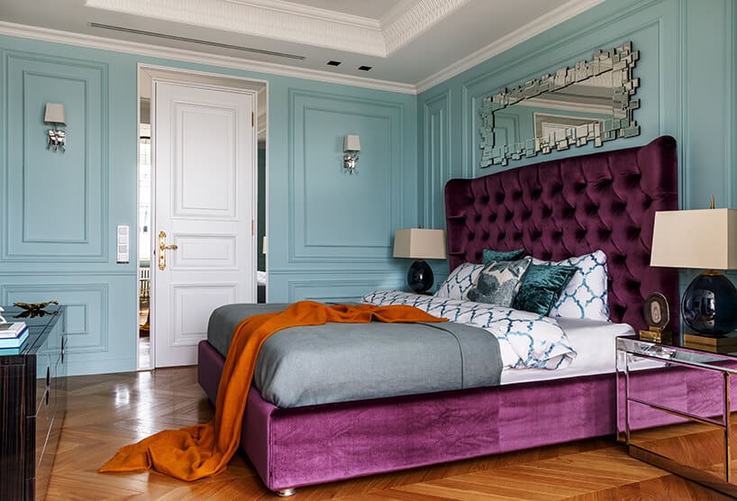 elegancka niebieska sypialnia z dużym fioletowym łóżkiem z wysokim oparciem pod wyjątkowym lustrem