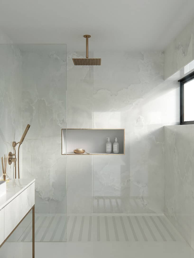 łazienka wykończona białym kamieniem od Cosentino ze złotą deszczownią i półką wykończoną złotą listwą