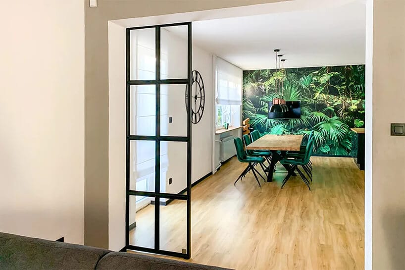 duży salon oddzielony szklanym czarnym parawanem w salonie z dużą zielenią na ścianie