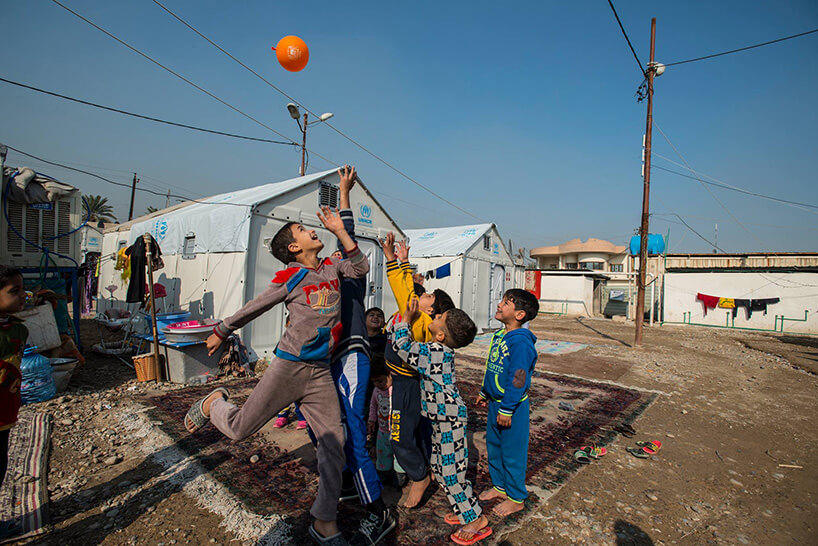 dzieci uchodźcy grający w piłkę przed barakami