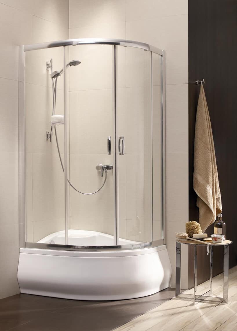 szklany prysznic z biała ceramiczną wanną stoliczek z kosmetykami brązowy ręcznik na ścianie z płytek