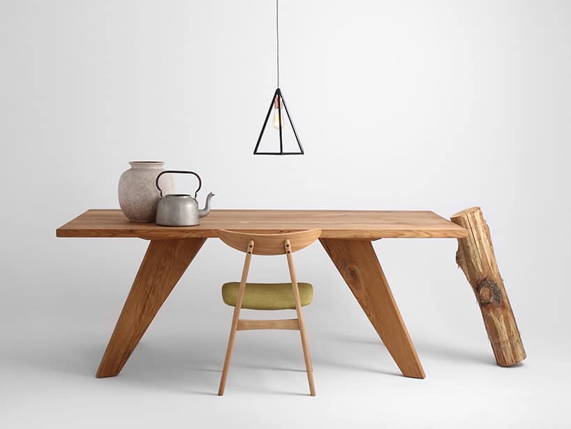 drewniany stół na drewnianych skośnych nogach pod prosta czarną lampą z metalowych czarnych prętów