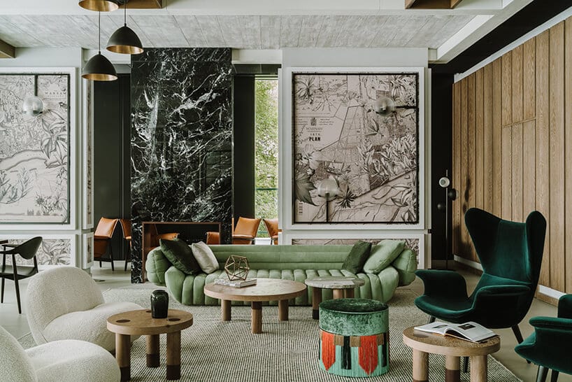 eleganckie wnętrze z zieloną sofą przy drewnianych stolikach na tle ściany z grafikami z elementami map śianką z czarnego kamienia