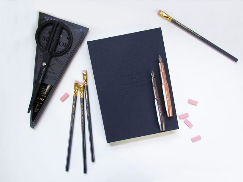 czarne nożyczki obok ołówków i piór na kalendarzu osobistym lezące na białej powierzchni