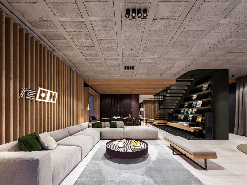 projekt nowoczesnego wnętrza domu od Zarysy salon z dużą modułową sofą obok czarnej ściany ze schodami i zabudowanymi półkami