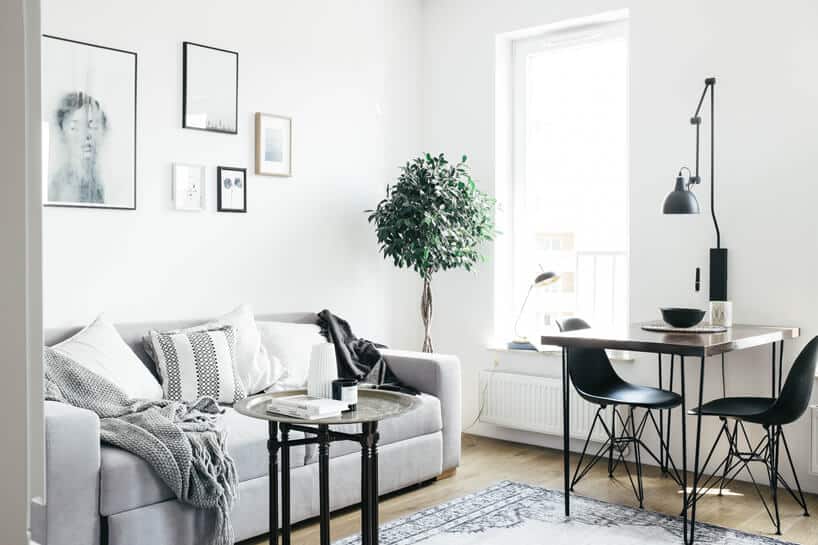 białe wnętrze salonu w stylu skandynawskim od Odwzorowanie jasno szara sofa obok małego stolika z ciemnym blatem