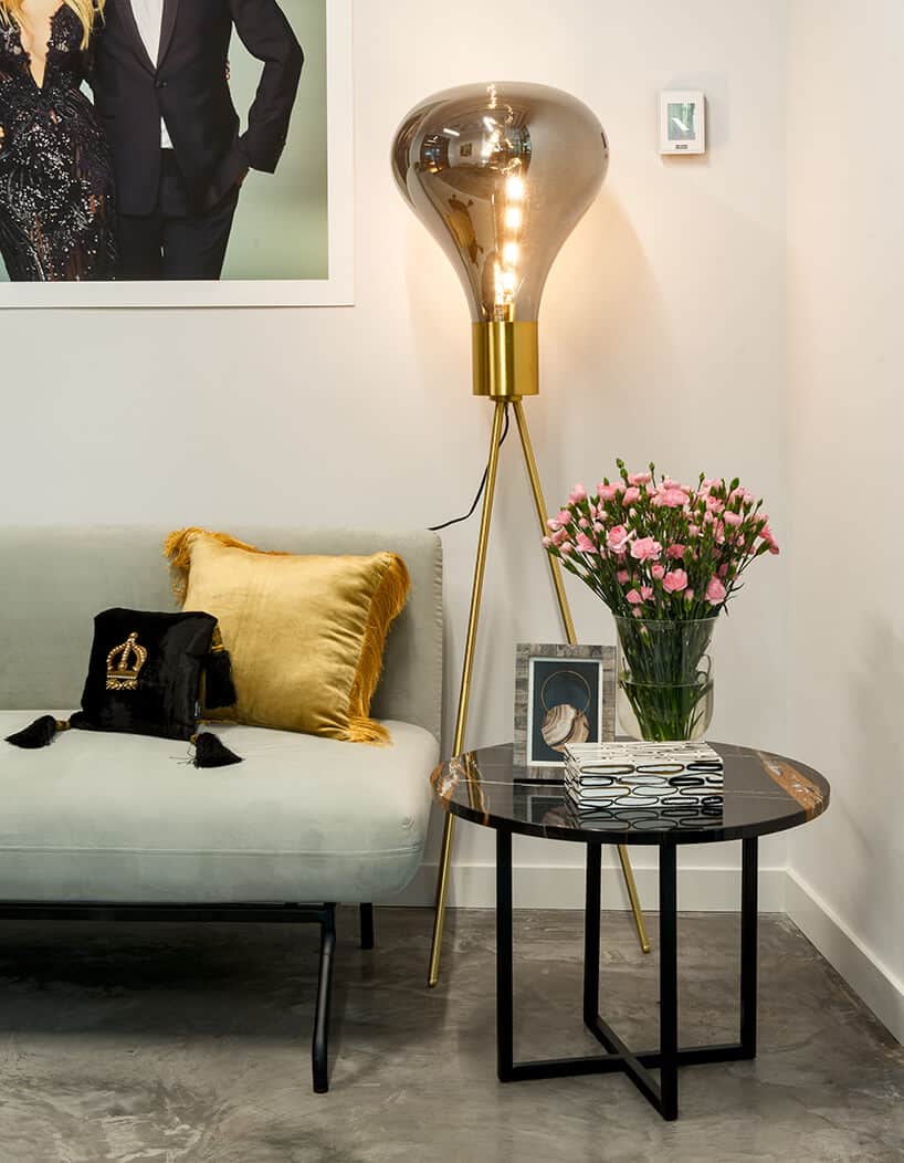nowe atelier Paprocki & Brzozowski efektowna wysoka złota lampa w kształcie żarówki obok szarego siedziska obok małego czarnego stolika