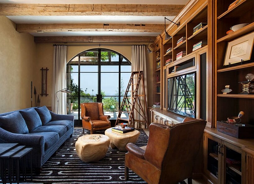 salon w stylu prowansalskim z drewnianą zabudową dużym oknem i niebieską sofą obok dwóch skórzanych foteli