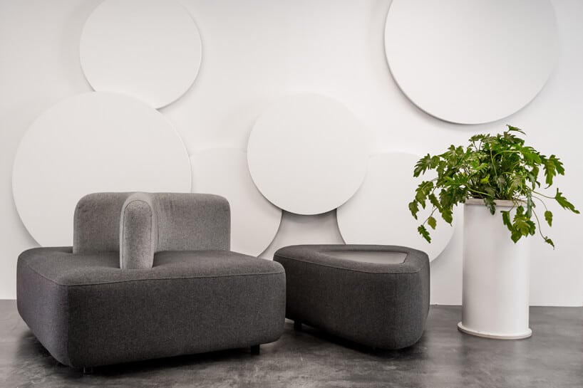 dwa szare nowoczesne siedziska obok wysokie donicy z kwiatem na tle białych okrągłyach dekaoracji na ścianie
