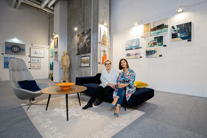 dwie kobiety Lena Szwed-Strużyńska i Ewa Mierzejewska siedzące na granatowej sofie w galerii Targów Sztuki Dostępnej