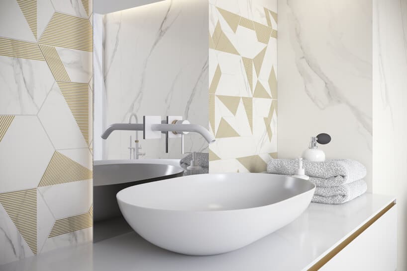 biała łazienka ze złotmi akcentami w płytkach z białą umywalką z wkomponowanym w duże lustro kranem