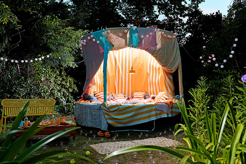 duża trampolina przykryta różnymi materiałami i zrobionymi baldachimami przerobiona na sypialnię