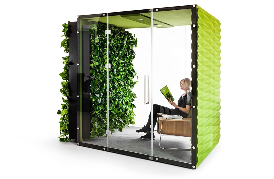 kobieta siedząca zielonym boxie akustycznym VANK_WALL JUNGLE z otwartymi szklanymi drzwiami i roślinami na zewnętrznej ścianie