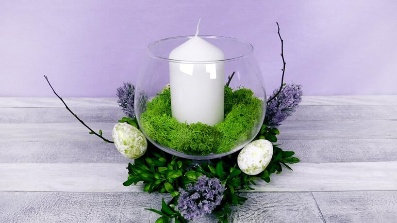 stroik wielkanocny ze szklanego wazonu z mchem i świecą w środku