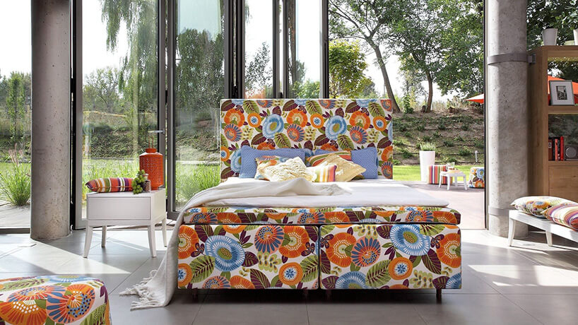 duże łóżko z tapicerką w wielkie kolorowe kwiaty